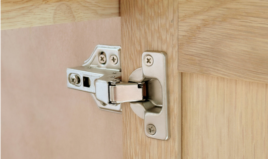 Close-up of soft-close hinge system mounted inside a cabinet, showing metal hardware against oak finish.